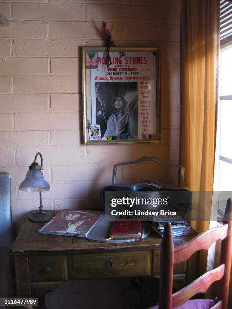 Desk in Gram Parsons' last room at the Joshua Tree Inn, poster for Rolling Stones at Altamont with visiting devotees' guitar picks tucked into the...