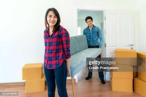 happy young asian couple lifting sofa or couch into bedroom with cardboard box at their new home together. moving house day. - new sofa stock pictures, royalty-free photos & images