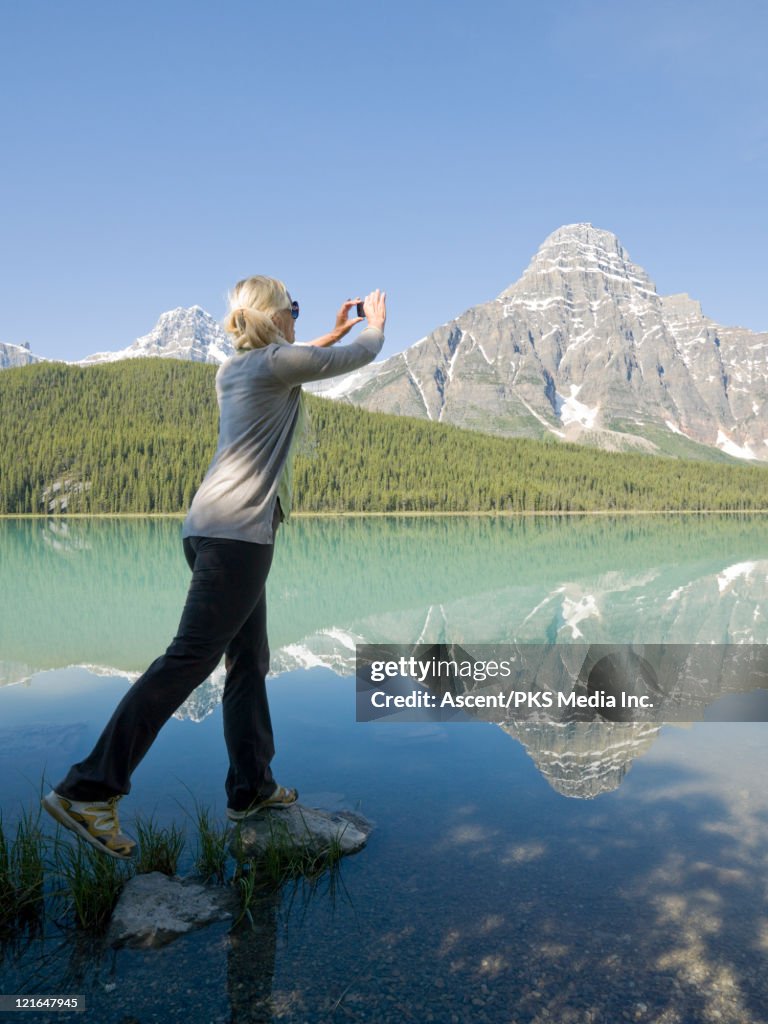 Woman takes cell phone picture of mtn lake