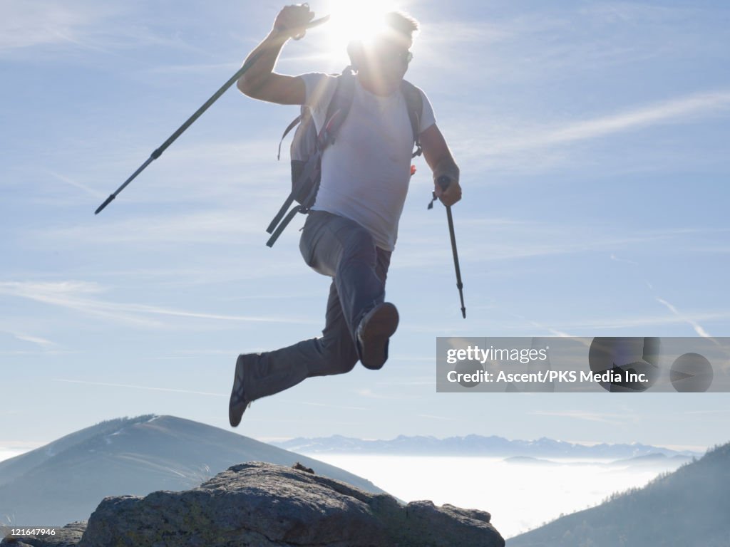 Hiker in mid-air leap between rocks, mtns below