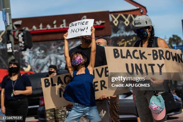 Girl jumps holding a sign while she and her family protest in the Boyle Heights neighborhood of Los Angeles on May 30, 2020 in response against the...
