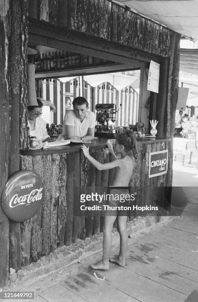 Little girl buys a drink at a bar on Paraggi Beach, near the tourist resort of Portofino, Italy, August 1952. Original Publication : Picture Post -...