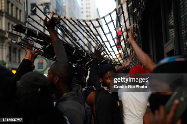 People hold open a metal gate to gain access to a store on Walnut Street, in Philadelphia, PA on May 30, 2020. Protestors clash with police in cities...