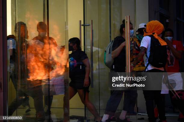 As people gain access flames from a police car set ablaze are reflected in the glass doors of the Apple Store on Walnut Street, in Philadelphia, PA,...