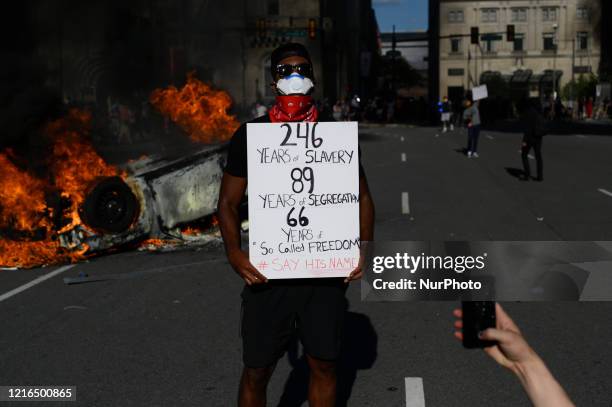 An African-American male poses with a sing in front of burning and overturned police cruiser as protestors clash with police near City Hall, in...