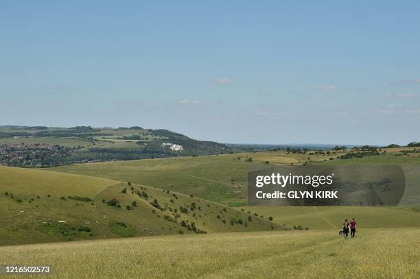 People walk their dog on Mount Caburn, a prominent high point on the South Downs east of Lewes in southern England on May 31, 2020 on the eve of a...