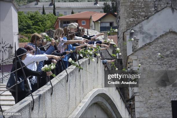 People wearing white ribbons on their arms in memory of the civilians killed in wartime by Serbs in city of Prijedor, throw white roses from the...