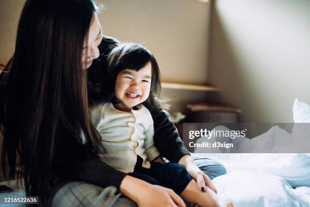 cute little daughter smiling joyfully and sitting on mother's lap after waking up in the morning - japanese mom stock pictures, royalty-free photos & images