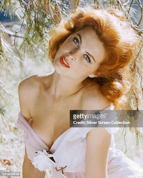Tina Louise, US actress and singer, wearing a white tope, which has fallen down from her shoulders, with a white flower on the front, circa 1960.