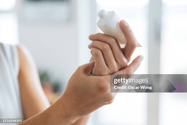close up shot of young woman rubbing hand sanitiser on hand to prevent spreading of the coronavirus ( covid-19) - rubbing hands together stock pictures, royalty-free photos & images