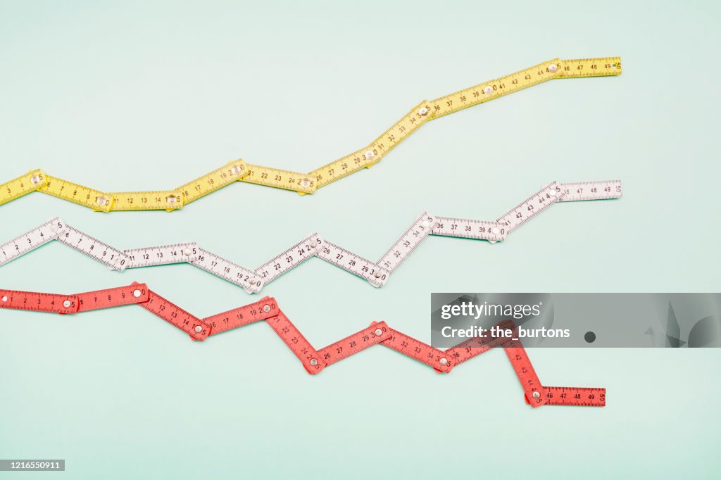 High angle view of folding rulers in shape of a stock curve on turquoise background