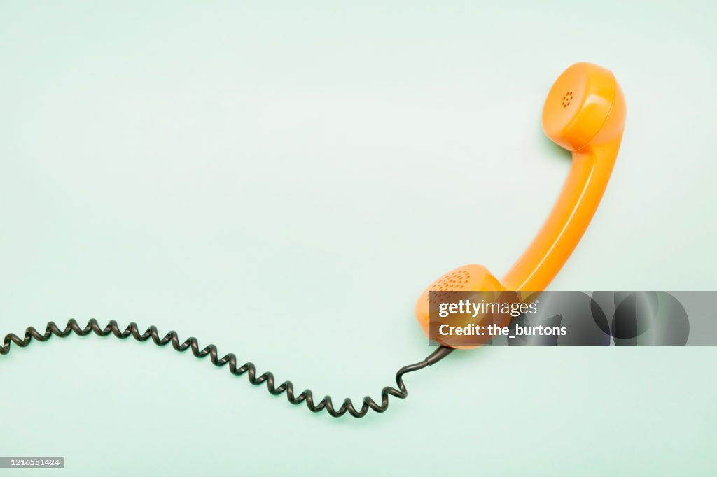 High angle view of an orange old-fashioned telephone receiver on turquoise background