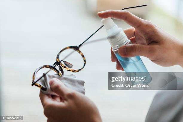 close up shot of woman cleaning eyewear surface with sanitising spray - 2020 eyeglasses stock pictures, royalty-free photos & images