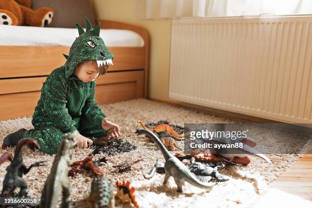 adorable toddler boy in a dinosaur costume playing with his toys - playroom stock pictures, royalty-free photos & images