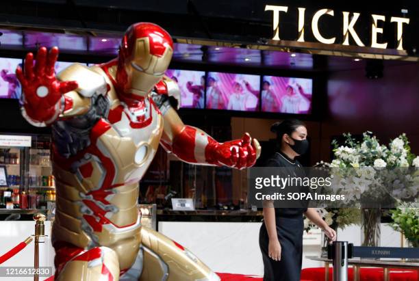 Theater worker walks past a steel and brass statue of Iron Man while wearing a face mask as a preventive measure in a movie theater during the...