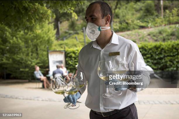 An employee wearing protective gloves and a mask carries glasses of wine at the Buena Vista Winery tasting area in Sonoma, California, U.S., on...
