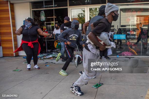 People run with items looted in a clothing store in downtown Long Beach on May 31, 2020 during a protest against the death of George Floyd, an...
