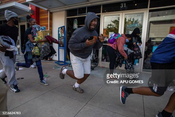 People run with items looted in a clothing store in downtown Long Beach on May 31, 2020 during a protest against the death of George Floyd, an...