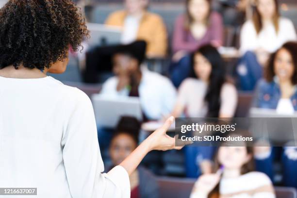 unrecognizable female professor gestures while teaching diverse college students - auditorium stock pictures, royalty-free photos & images