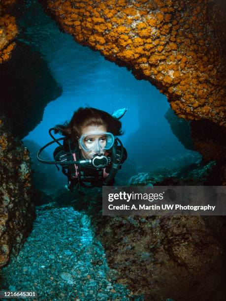 young girl doing scuba-diving and exploring an underwater cave with walls covered by orange coral. - scuba mask stockfoto's en -beelden