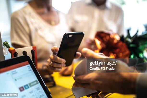 senior woman paying by mobile in a store - loja-de-conveniência imagens e fotografias de stock