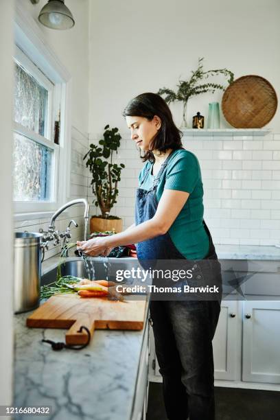 pregnant woman washing vegetables at sink in kitchen - women with health faucet stock pictures, royalty-free photos & images