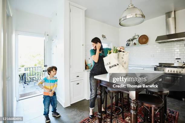 pregnant mother bringing groceries in canvas bags into kitchen with young son - jeans latzhose frau stock-fotos und bilder