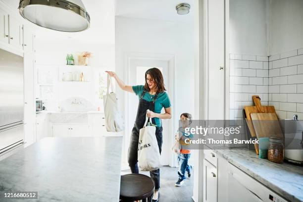 pregnant mother bringing groceries in canvas bags into kitchen with young son - kitchen bench top stock pictures, royalty-free photos & images