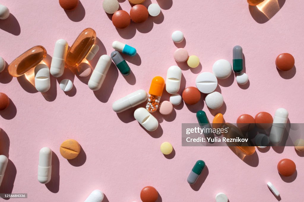 Top view of spoon with various pills and tablets on the pink background