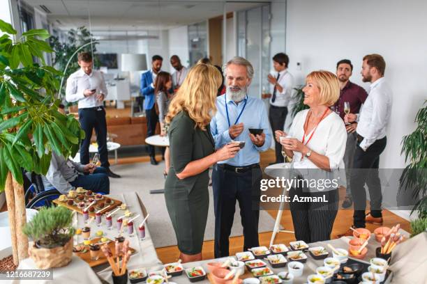 leende kollegor njuter av mat och konversation på fest - launch event bildbanksfoton och bilder