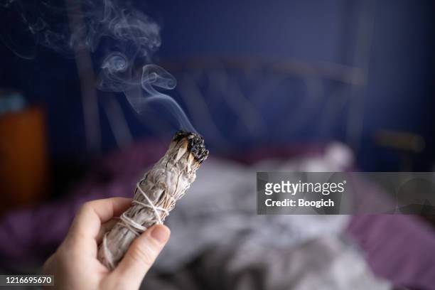 woman cleansing the air by smudging burning sage indoors in miami florida - burning sage stock pictures, royalty-free photos & images