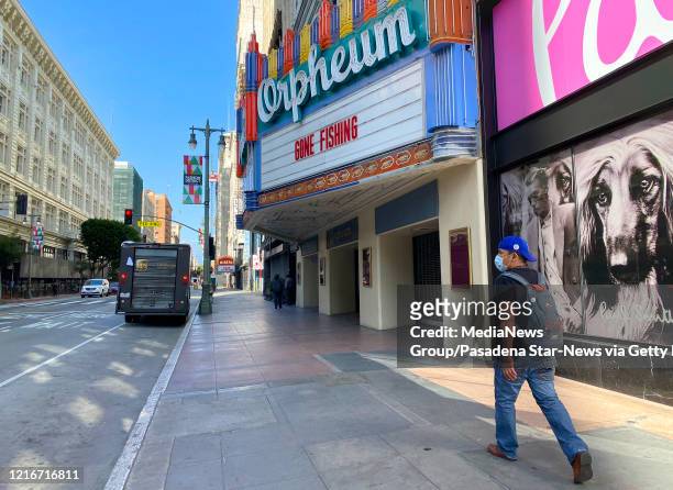 Man wearing a mask walks past the Orpheum Theatre where the marque sign says Gone Fishing along Broadway during the Coronavirus Pandemic in Los...