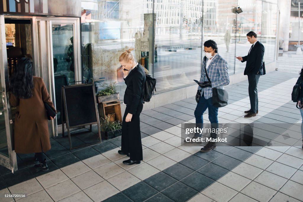 People standing in line outside cafe keeping distance