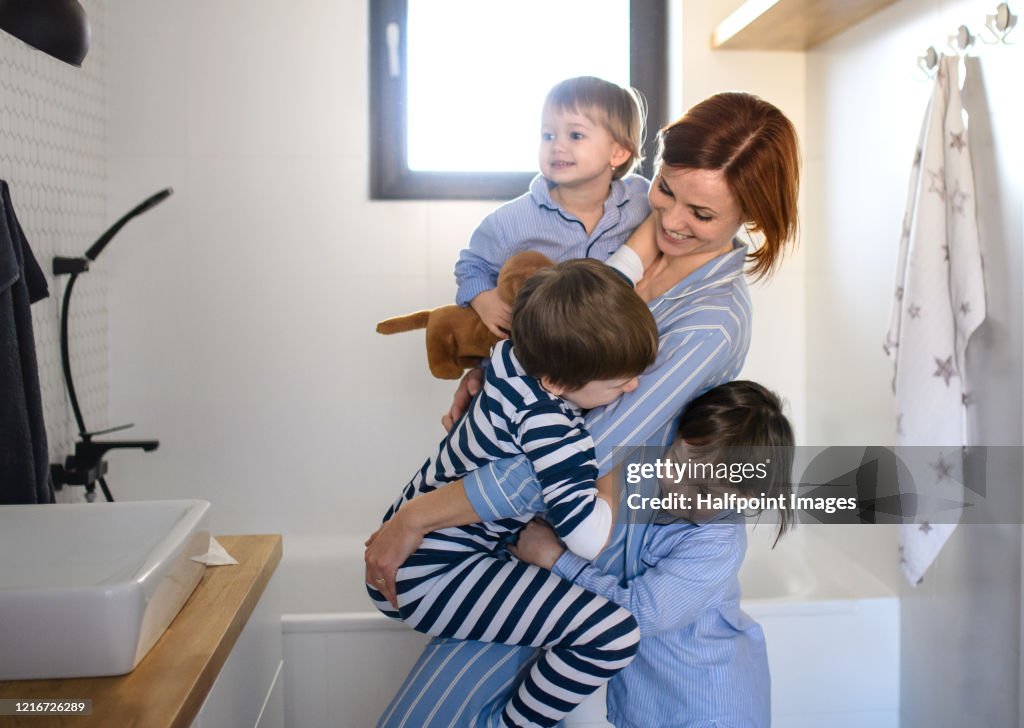 Mother with small children indoors in bathroom in the morning at home, having fun.