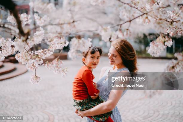 mother holding young girl under cherry blossoms, tokyo - eurasische herkunft stock-fotos und bilder