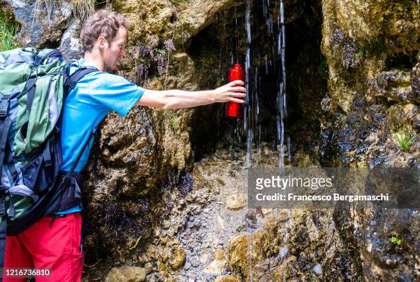 hiker collects water with a red bottle from a small waterfall. - bergamo stock photos et images de collection