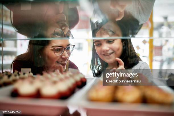 moeder en dochter die cupcakes van vertoningsgeval selecteren - boulangerie vitrine stockfoto's en -beelden