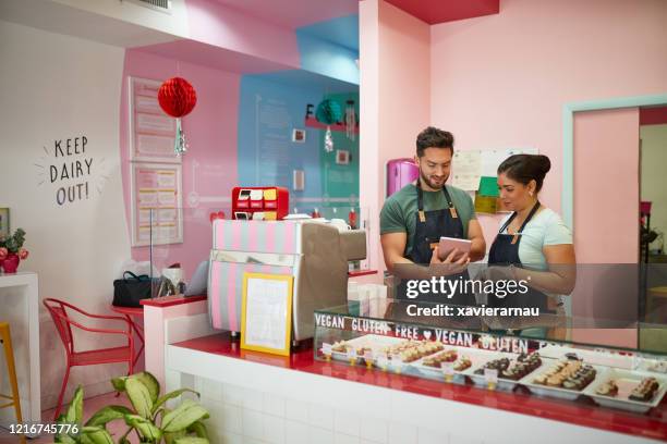 bakery employees using digital tablet at checkout counter - america patisserie stock pictures, royalty-free photos & images