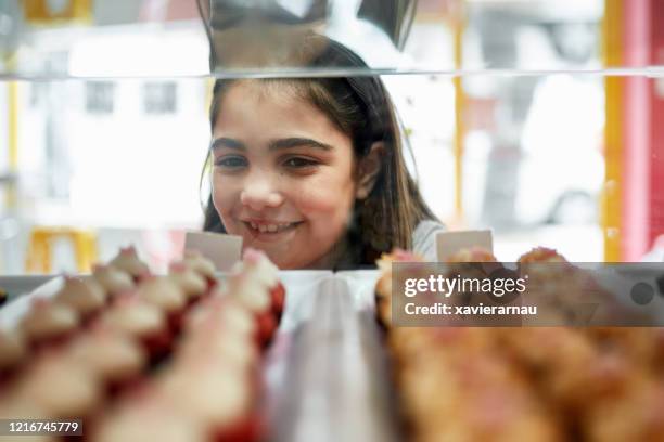 hispanic girl looking at red velvet cupcakes in display case - cake case stock pictures, royalty-free photos & images