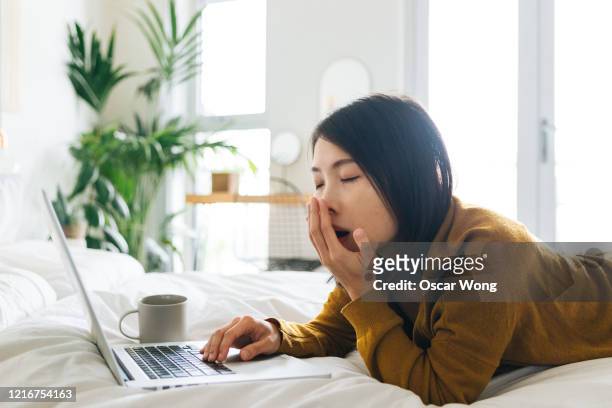 young woman yawning when using laptop working from home - yawning is contagious stock-fotos und bilder