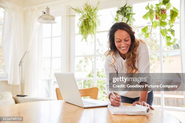 smiling mature woman writing notes while standing at a table at home - polynesian ethnicity stock pictures, royalty-free photos & images
