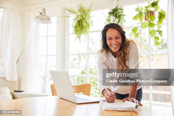 lächelnde reife frau schreibt notizen während der arbeit von zu hause - einzelne frau über 40 stock-fotos und bilder