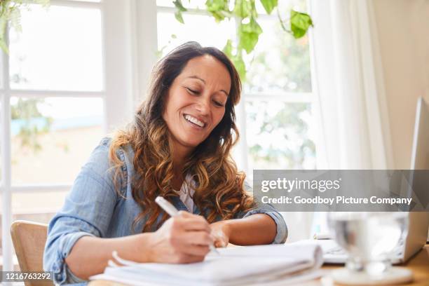 donna matura sorridente che scrive in un quaderno mentre lavora da casa - notebook smiling business foto e immagini stock