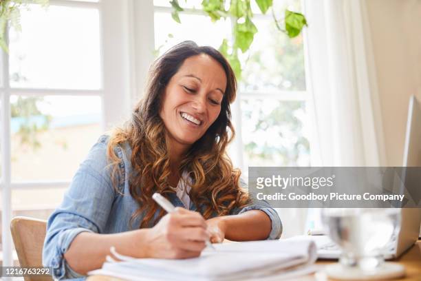 smiling mature woman writing in a notebook while working from home - writing stock pictures, royalty-free photos & images
