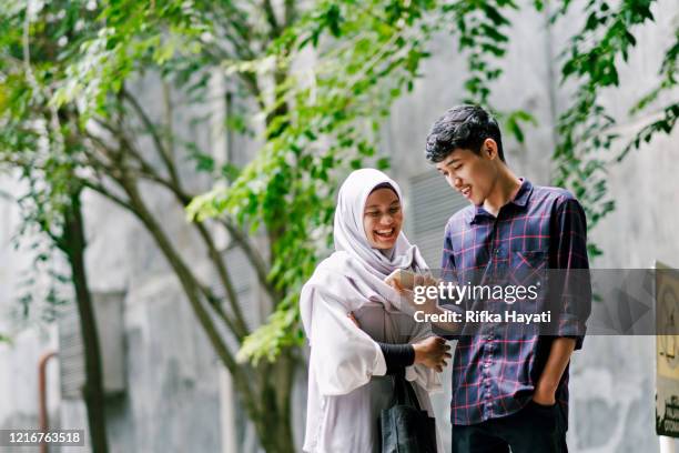 giovane bella coppia musulmana guardando il telefono cellulare insieme mentre cammina - indonesian ethnicity foto e immagini stock