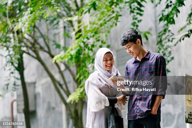 young beautiful muslim couple looking at mobile phone together while walking - malay couple stock pictures, royalty-free photos & images