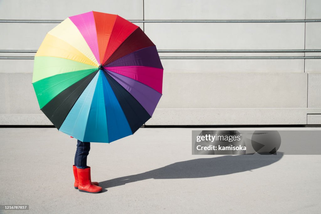 Stehendes Mädchen mit buntem Regenschirm vor einer Betonwand