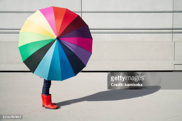 ragazza in piedi con ombrello multicolore di fronte a un muro di cemento - protezione foto e immagini stock