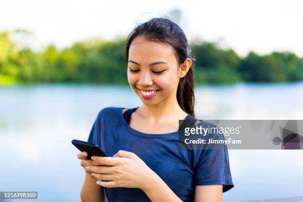 young asian fitness woman using mobile phone by a lake - philippines women stock pictures, royalty-free photos & images