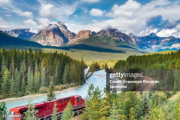 red train at morant's curve, banff national park, canadian rockies, canada - montañas rocosas canadienses fotografías e imágenes de stock